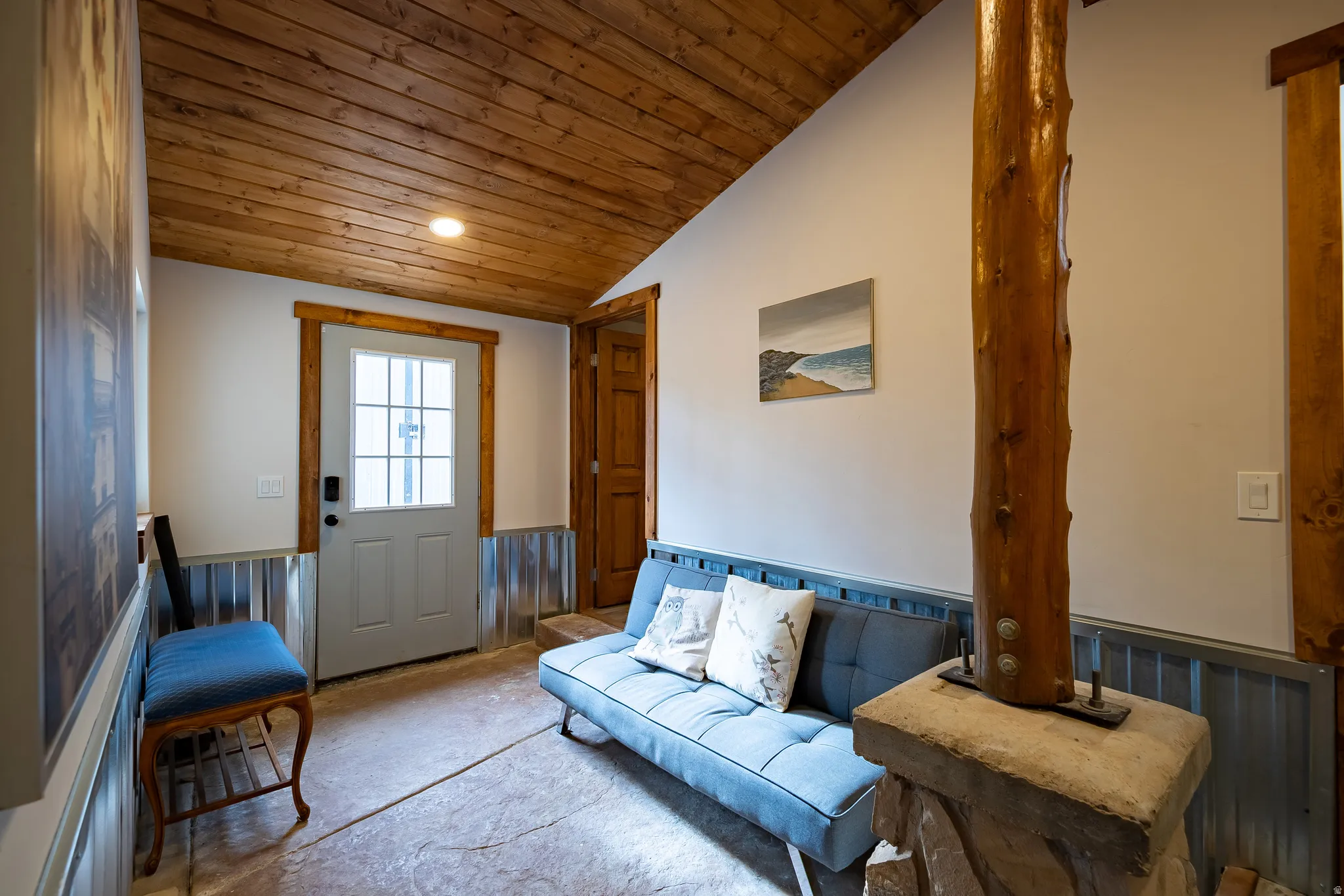 Vaulted wood-plank ceiling, concrete-style flooring, paneled door with glass inserts, wood-trimmed doorway, and corrugated metal wainscoting