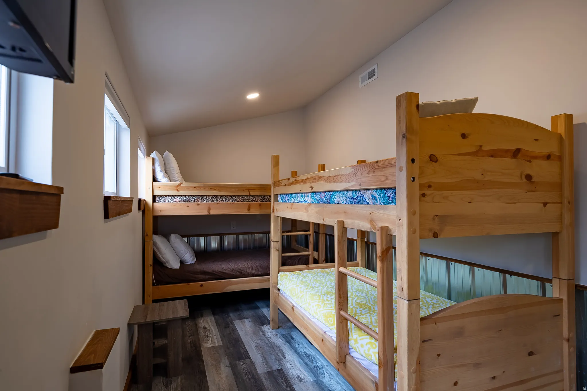 Sloped ceiling room featuring two wooden bunk beds, recessed lighting, wood-finish flooring, and two windows with wood sills