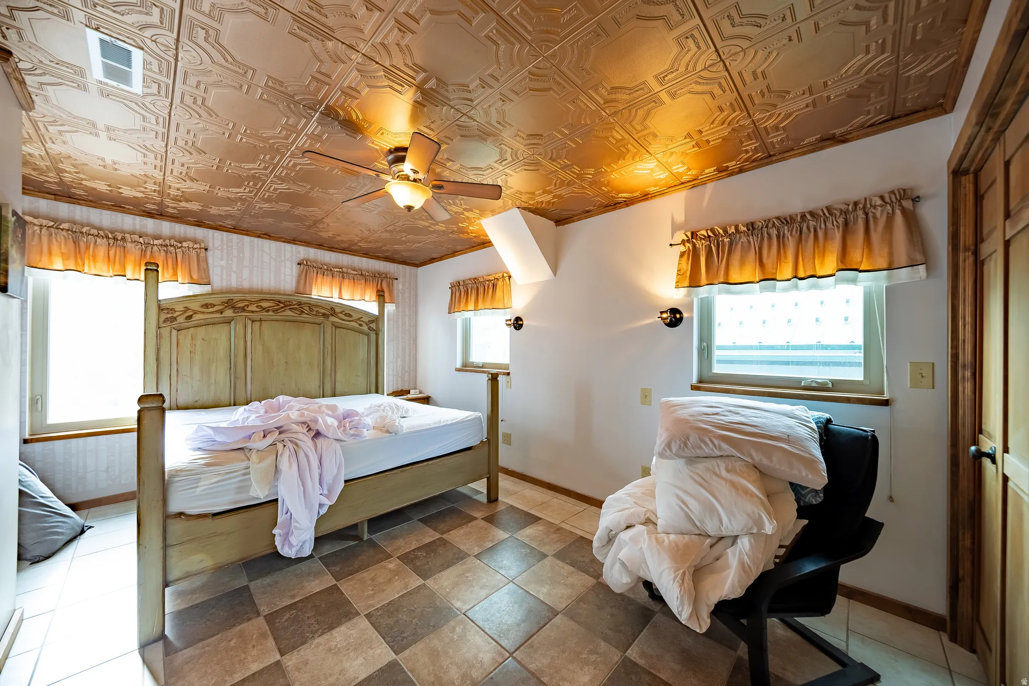 Ornate textured ceiling, integrated ceiling fan with lighting, checkerboard tile flooring, dual wall sconces, and natural wood-finish trim