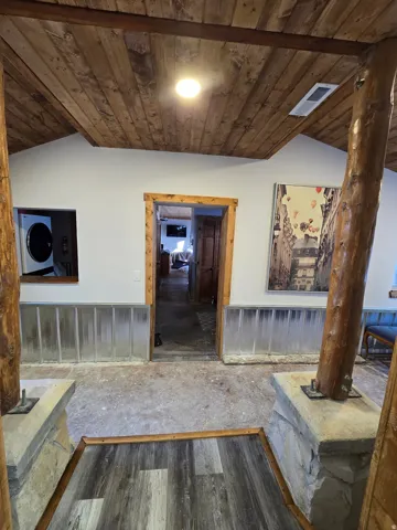 Wood-finish plank ceiling with exposed beams, stone base columns, and wood-trimmed doorways