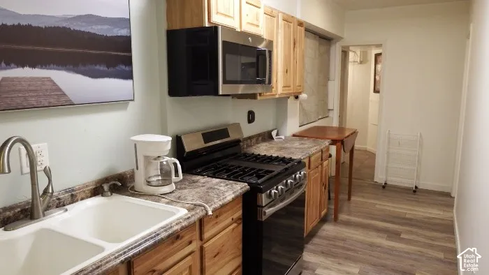 Compact kitchen featuring wood-finish cabinetry, stainless steel microwave, gas range, and a double basin sink