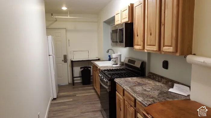 Galley kitchen featuring wood-finish cabinetry, stainless steel appliances, and wood-finish flooring