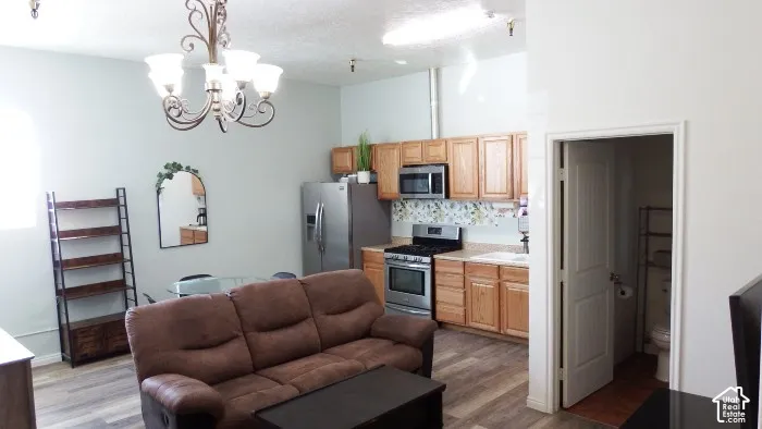 Vaulted ceiling, wood-finish flooring, stainless steel appliances, wood cabinetry, and a decorative chandelier