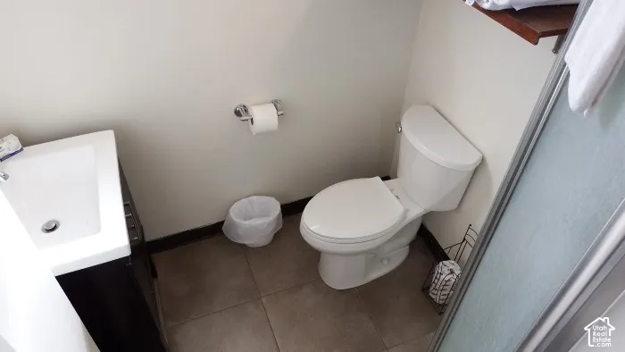 White ceramic toilet, dark wood-finish vanity with integrated sink, and tiled flooring