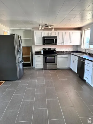 Spacious kitchen featuring gray tile flooring, white shaker cabinetry, dark countertops, a white subway tile backsplash, and stainless steel appliances