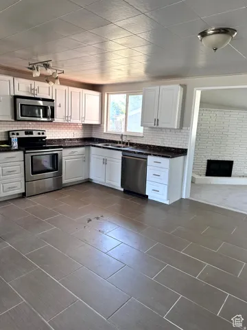 Contemporary kitchen featuring white cabinetry, stainless steel appliances, dark countertops, and a white subway tile backsplash