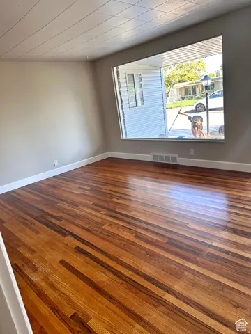 Hardwood flooring with varied wood tones, neutral wall paint, and a large bay window