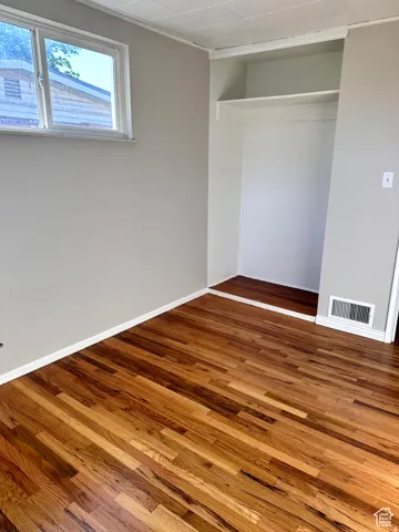 Hardwood flooring, painted walls, white trim, open closet with shelving, and a window for natural light