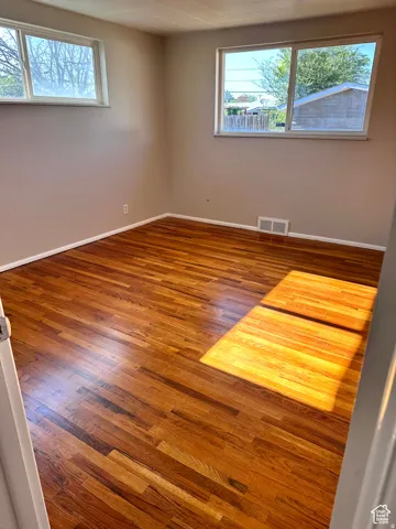 Hardwood flooring throughout, two large windows, white trim, and neutral wall tones