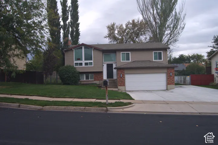 Split-level exterior featuring tan horizontal siding, red brick accents, an attached two-car garage, and large multi-pane windows