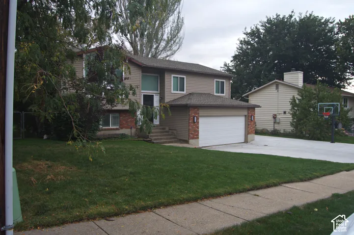 Two-story exterior featuring tan horizontal siding, brick masonry accents, an attached two-car garage, and a concrete driveway