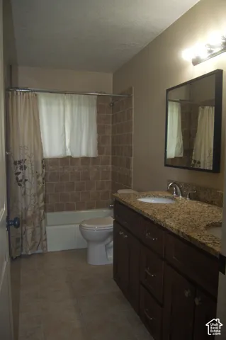Bathroom featuring a dual-sink vanity with stone-surfaced countertop, dark-finish cabinetry, tile-surround shower and tub combination, and ceramic tile flooring