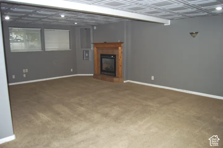 Expansive room featuring neutral carpeting, a wooden mantel fireplace with an insert, decorative ceiling tiles, and recessed lighting