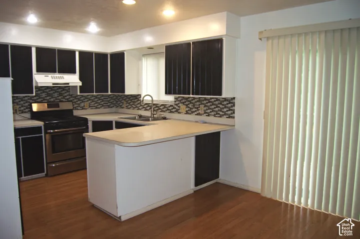 Kitchen featuring contrast cabinetry, stainless steel range with overhead vent, wood-finish flooring, patterned tile backsplash, and recessed lighting
