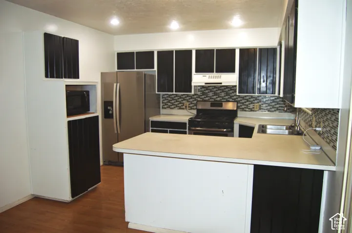 Kitchen featuring two-tone cabinetry, stainless steel refrigerator, mosaic tile backsplash, wood-finish flooring, and recessed ceiling lighting