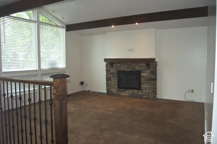 Vaulted ceiling featuring exposed dark wood beams, floor-to-ceiling windows, stone fireplace with a thick wood mantel, and wrought iron railings