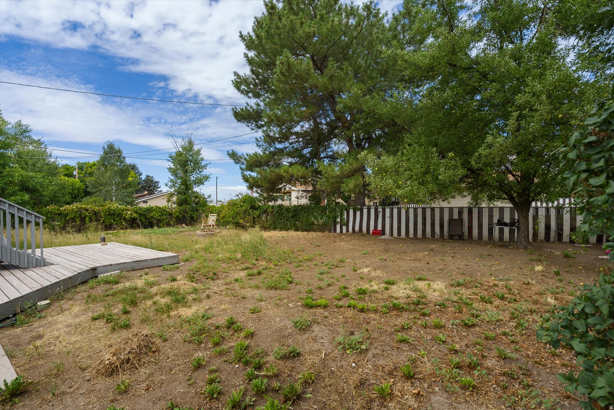 Spacious backyard with mature tree canopy, wooden deck platform, and sturdy perimeter fencing