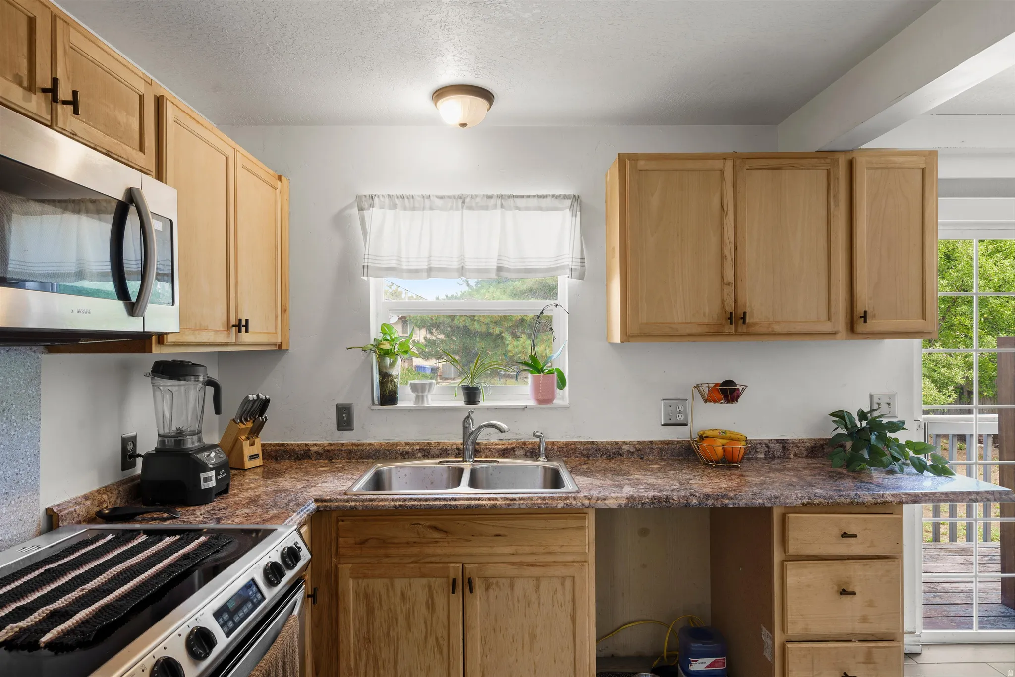Stainless steel microwave, double basin sink, natural wood-finish cabinetry, and textured countertops