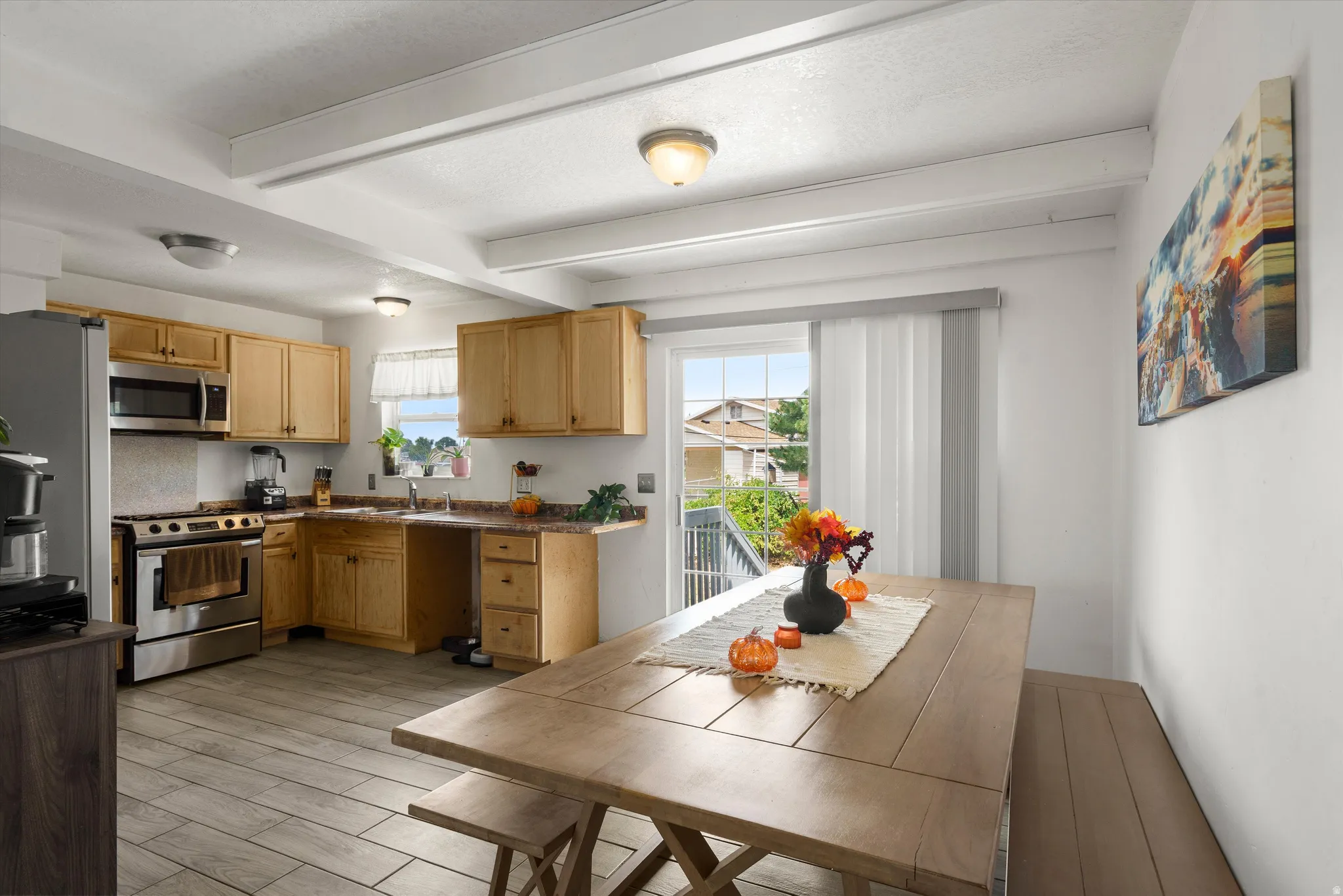 Bright, open-concept kitchen and dining area featuring natural wood cabinetry, stainless steel appliances, tile flooring, and abundant natural light from multiple windows