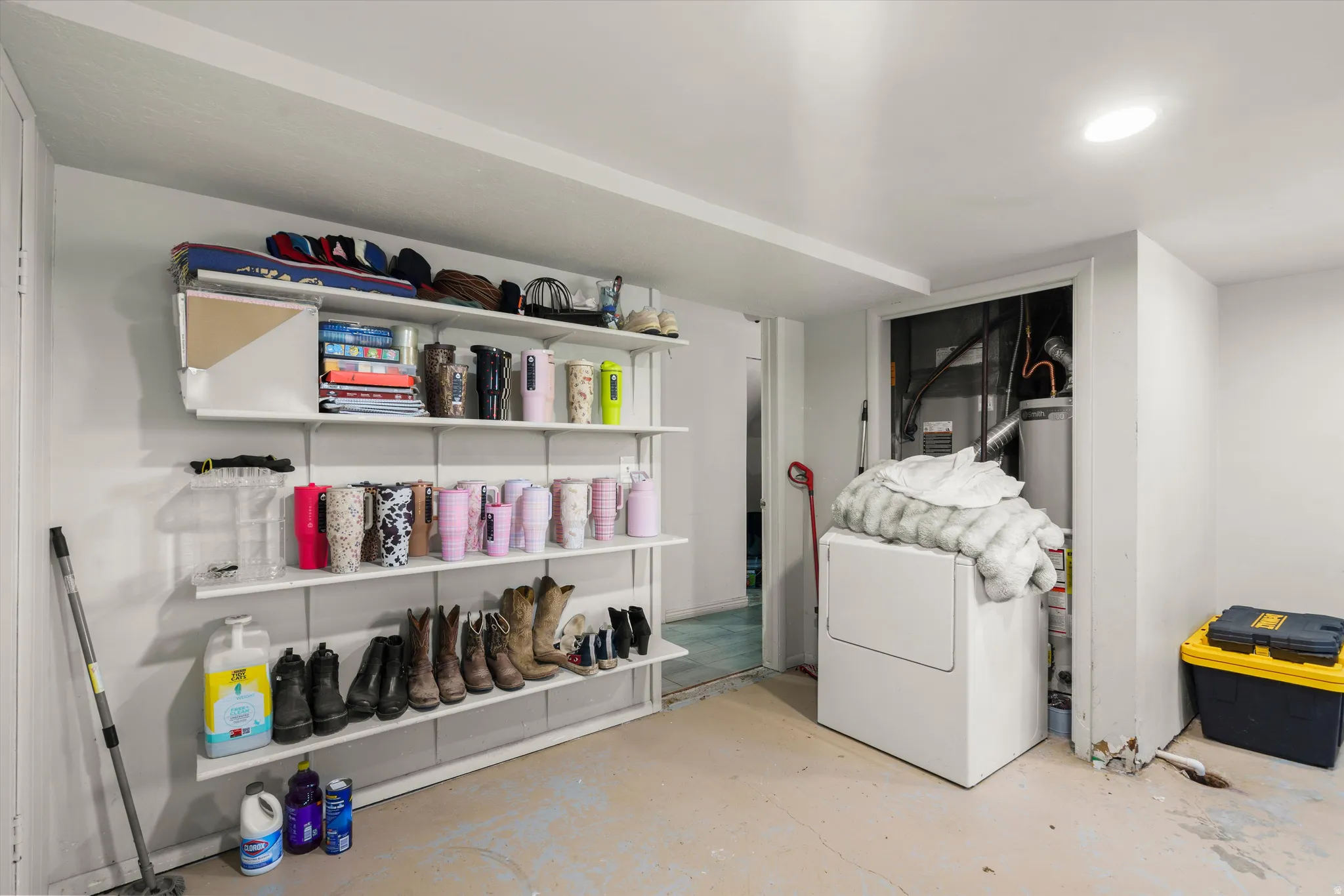 Utility room featuring wall-mounted shelving with organizational compartments for storage, laundry appliances including a front-load washer and dryer, concrete flooring, and recessed ceiling lighting