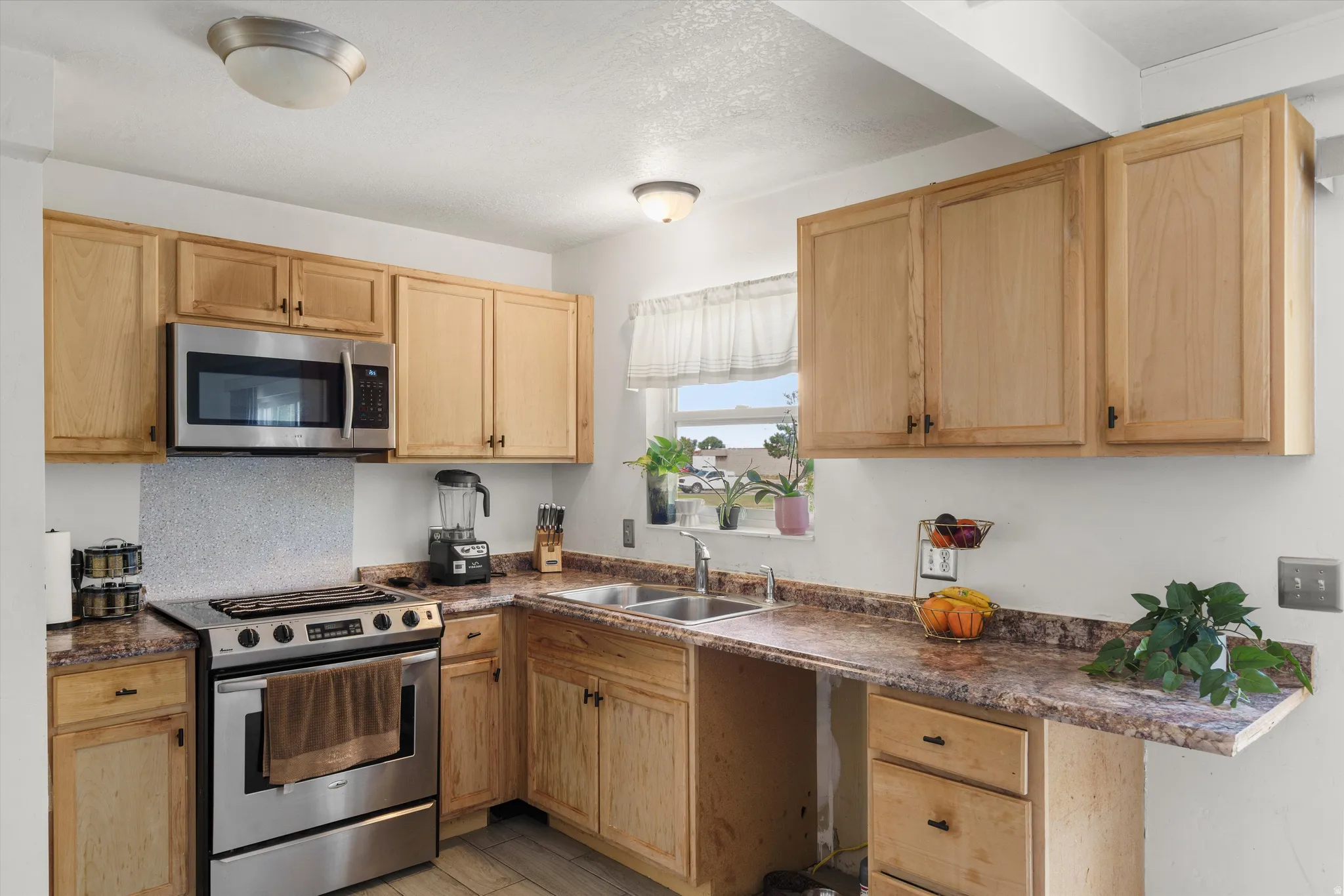 Kitchen featuring wood cabinetry, stainless steel microwave, stainless steel range, and a double basin sink