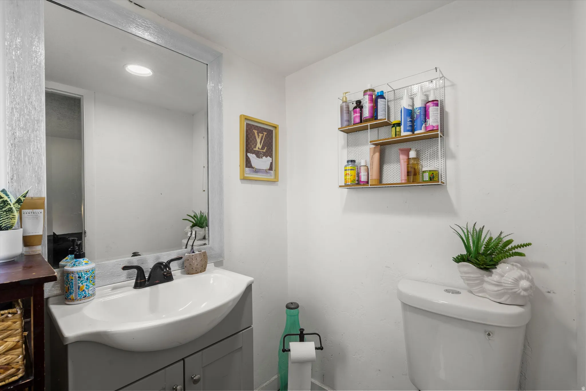 Vanity with an integrated sink and base cabinet, framed mirror, wall-mounted shelving unit, and a toilet with a top-mounted flush
