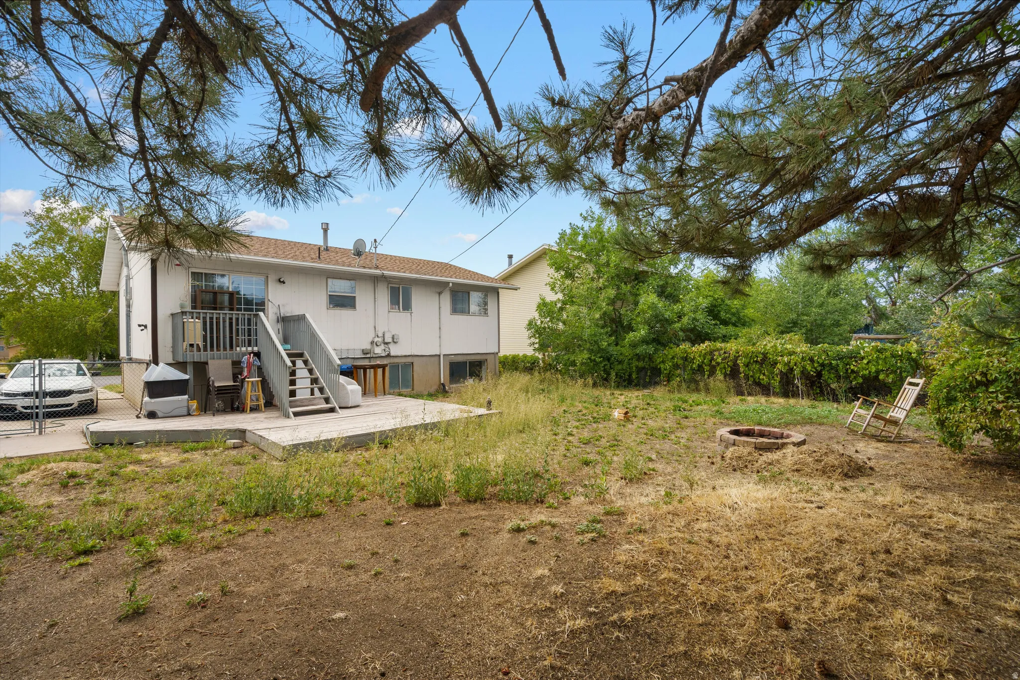 Spacious residential property featuring a two-story white exterior with multi-level deck access, mature tree canopy, and expansive grounds with natural landscaping and established vegetation