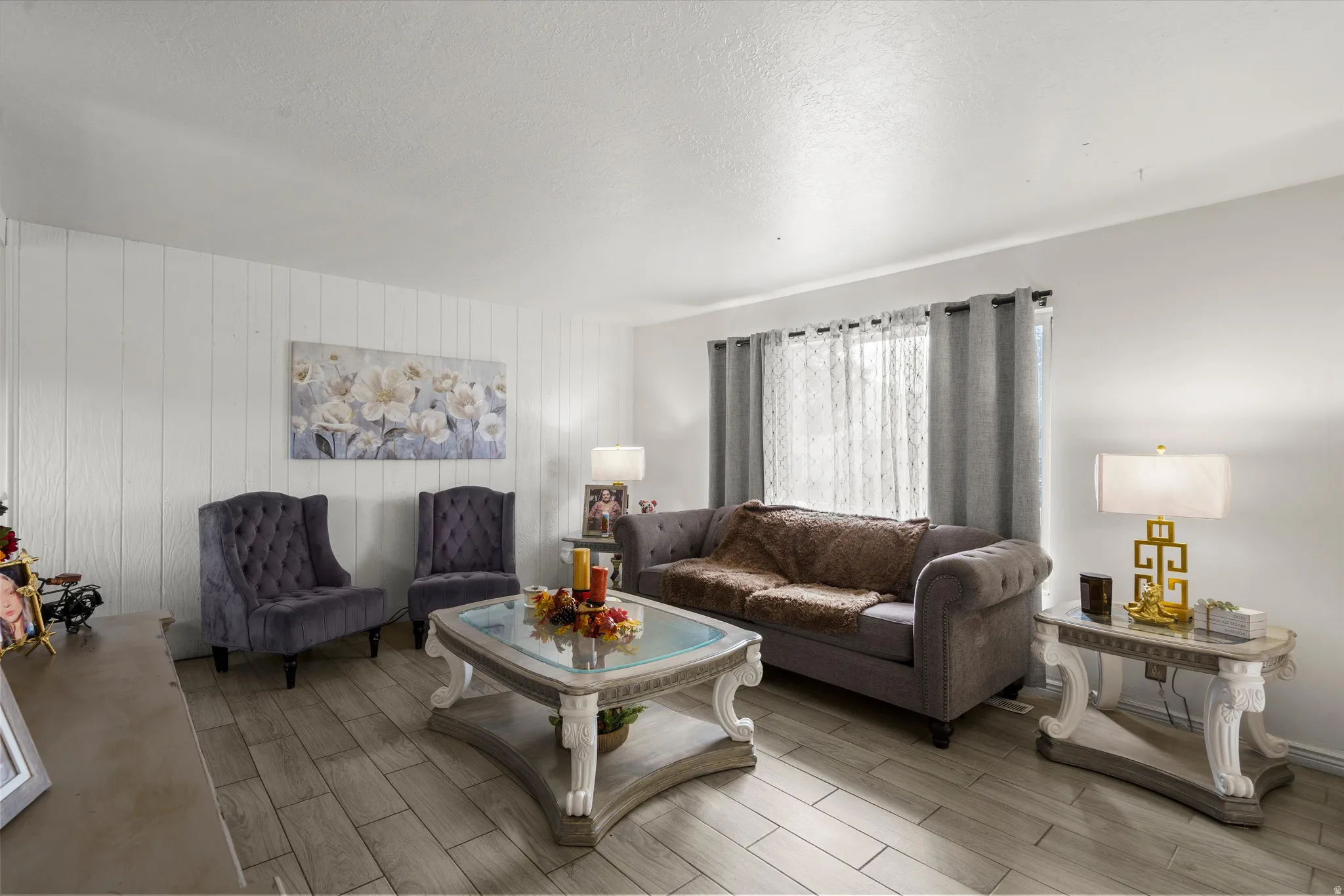 Wood-finish flooring, white panel accent wall, and a large window with privacy sheers