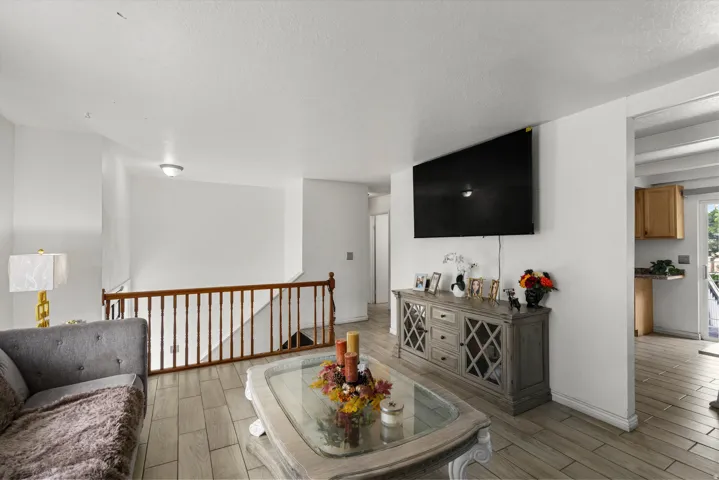 Wood-finish tile flooring throughout, white painted walls, and a wooden staircase with baluster railing