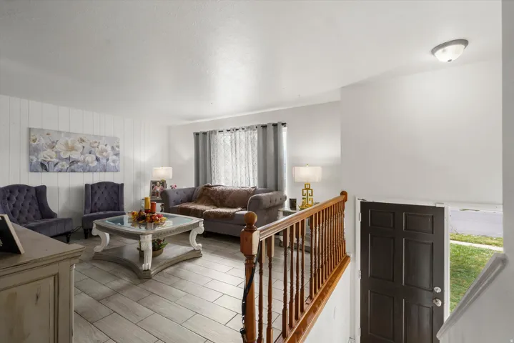 Recessed lighting, wood-finish flooring, white shiplap wall accent, dark wood banister, and a paneled entry door