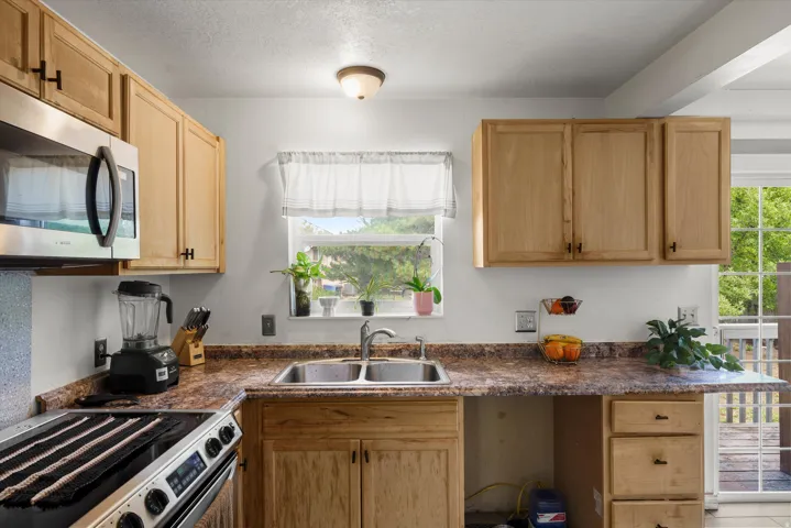 Stainless steel microwave, double basin sink, natural wood-finish cabinetry, and textured countertops