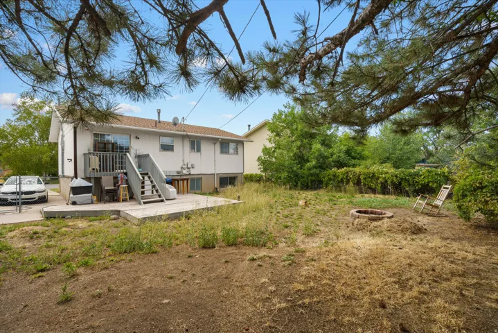 Spacious residential property featuring a two-story white exterior with multi-level deck access, mature tree canopy, and expansive grounds with natural landscaping and established vegetation