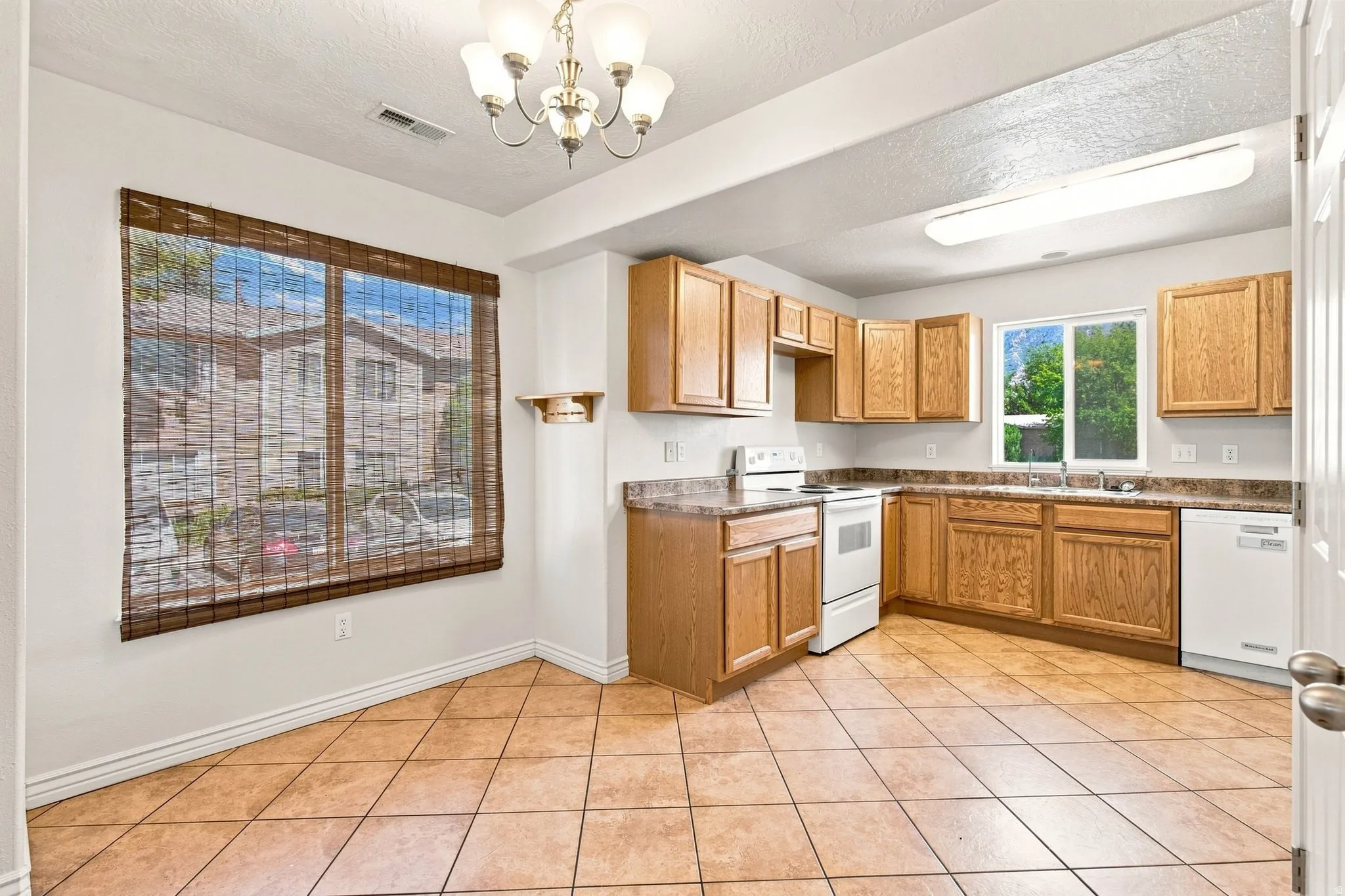 Main floor kitchen and dining area. The Kitchen featuring light wood-finish cabinetry, white appliances, and a double-basin stainless steel sink.