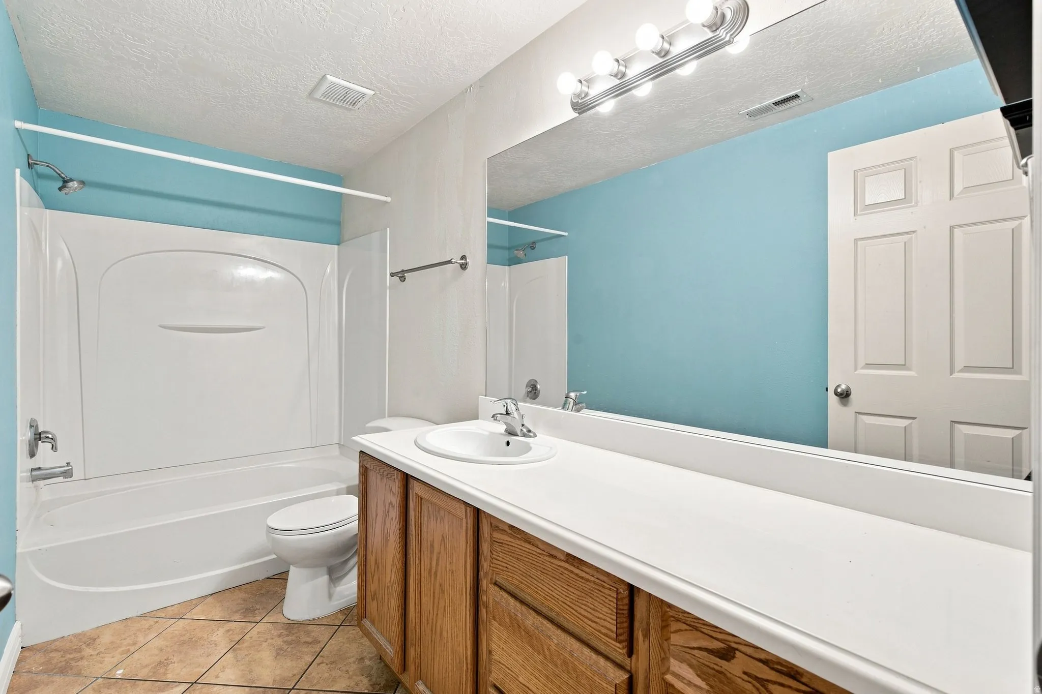 Bathroom featuring a full vanity with wood-finish cabinetry, a large mirror, a combined shower and tub, and tiled flooring