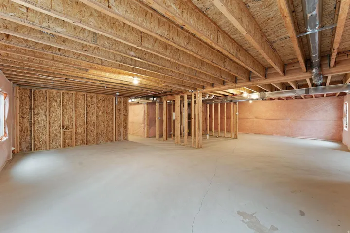 Unfinished basement with exposed wood joists and framing, concrete flooring, and visible ductwork