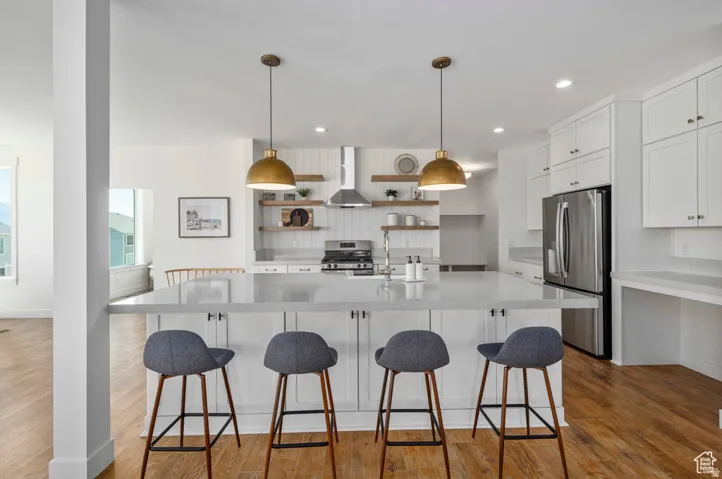 Spacious kitchen featuring an expansive central island, stainless steel appliances, white cabinetry, wood-finish flooring, and two pendant light fixtures