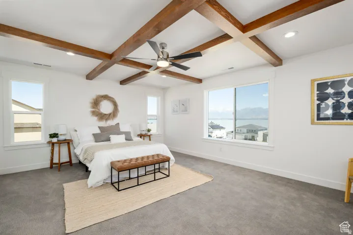Vaulted ceiling with exposed wood beams, ceiling fan, recessed lighting, expansive window with water scenery, and neutral carpeting