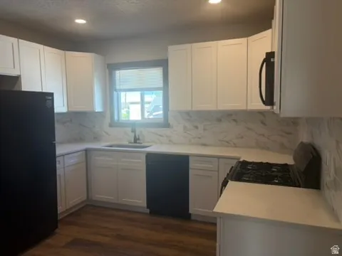 Kitchen featuring white shaker-style cabinetry, light-toned countertops, a full backsplash with a subtle veining pattern, a black gas range, and wood-finish flooring