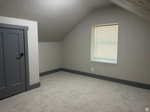 Carpeted flooring, sloped ceiling, window with blinds, paneled door, and dark trim