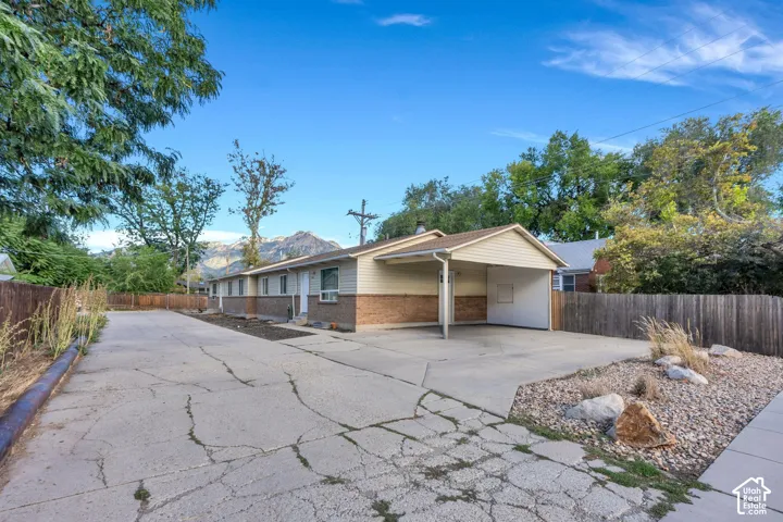 Exterior featuring brick and horizontal siding, attached carport, expansive concrete driveway, and wood fence enclosure