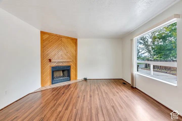 Wood-finish flooring, corner fireplace with chevron-patterned wood accent wall, tile hearth, and large horizontal window