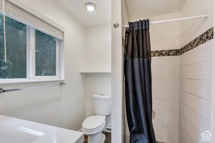 Bathroom featuring a vanity with a white countertop, a dual-flush toilet, a window with horizontal blinds, and a shower enclosure with white wall tiles and a honeycomb mosaic tile accent border