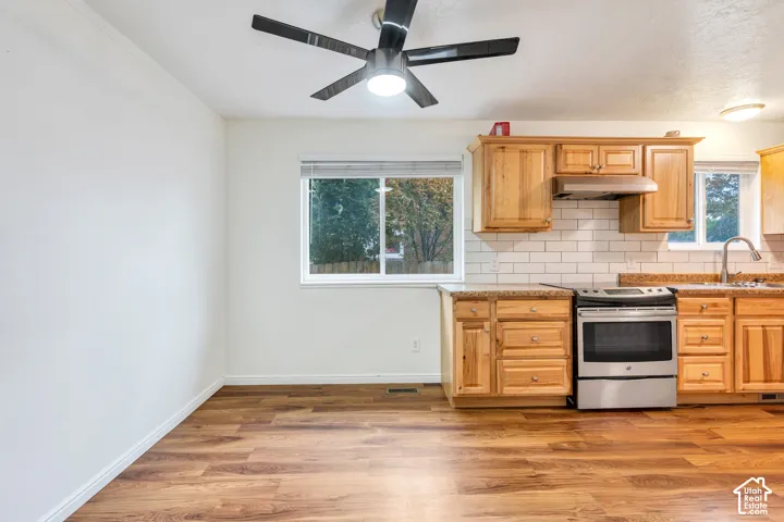 Kitchen featuring wood-finish cabinetry, subway tile backsplash, stainless steel range with overhead vent hood, and wood-finish flooring