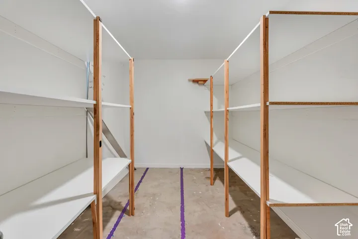 Storage space featuring white tiered shelving units with natural wood support posts and concrete flooring