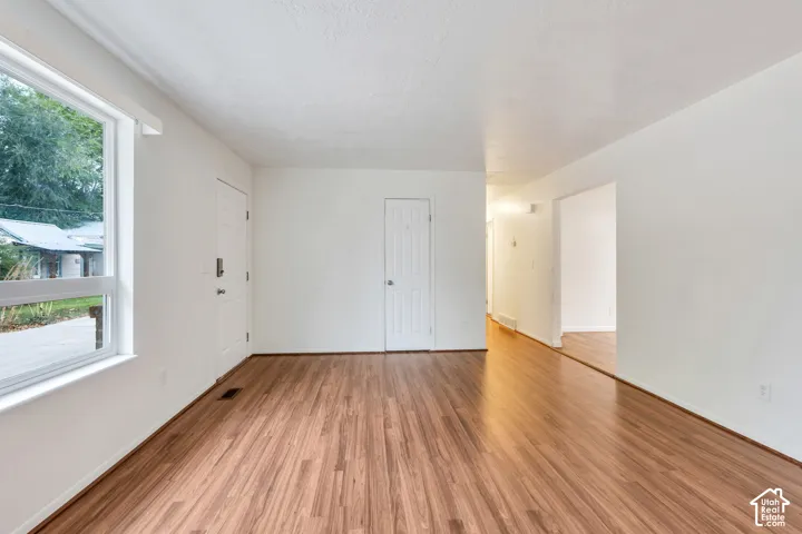 Interior space featuring wood-finish flooring, a large picture window, a solid-panel door, and smooth-finish white walls