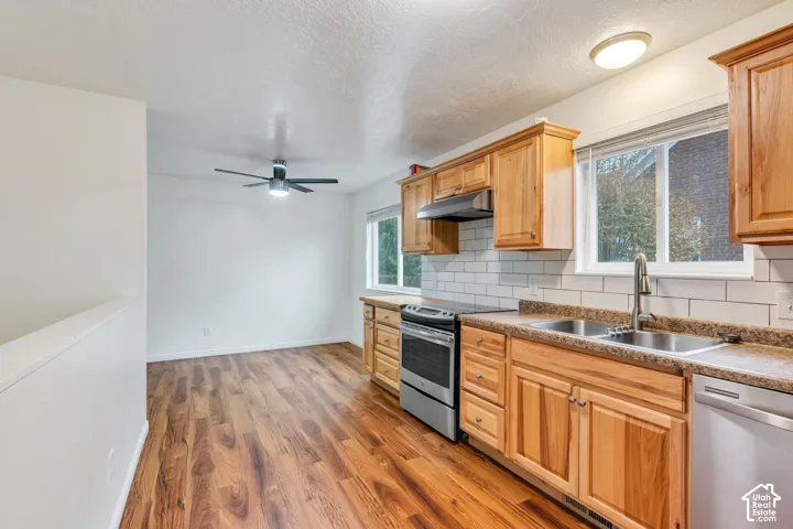 Kitchen featuring wood-finish cabinetry, stone-patterned countertops, stainless steel appliances, white subway tile backsplash, and wood-finish flooring