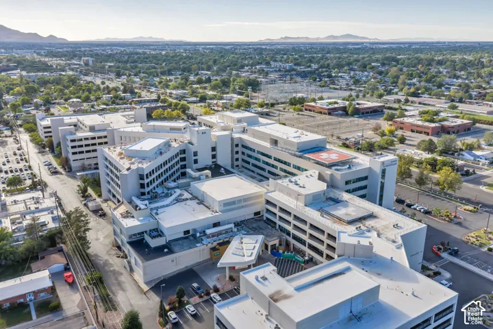 Multi-story complex featuring a flat roofline, integrated helipad, structured parking facility, and paved surface lots, set against a regional mountain backdrop