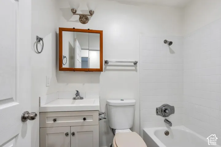 Bathroom featuring a white vanity with integrated basin, medicine cabinet, dual-light vanity fixture, and a tub with white tile surround