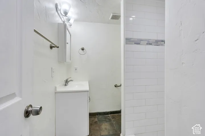 Bathroom featuring a vanity with an integrated sink, white subway-style wall tile with a decorative glass inlay, multi-toned stone-finish flooring, and a wall-mounted medicine cabinet