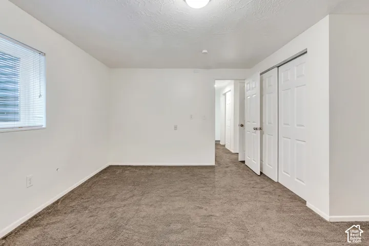 Interior space featuring neutral-toned carpeting, white walls, a rectangular window with blinds, and a built-in closet with multi-panel swinging doors